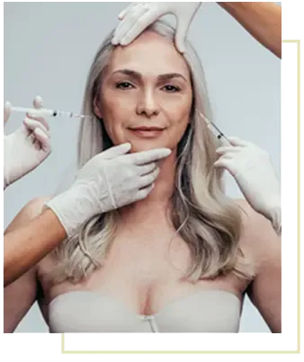 A woman looking at the camera while two gloved clinicians hold her face steady and prepare injections at her cheek and jawline.