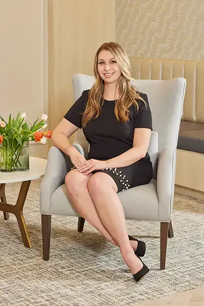 Courtney Carroll, licensed aesthetician, seated in an armchair in the NOOR Dermatology & Aesthetics office.